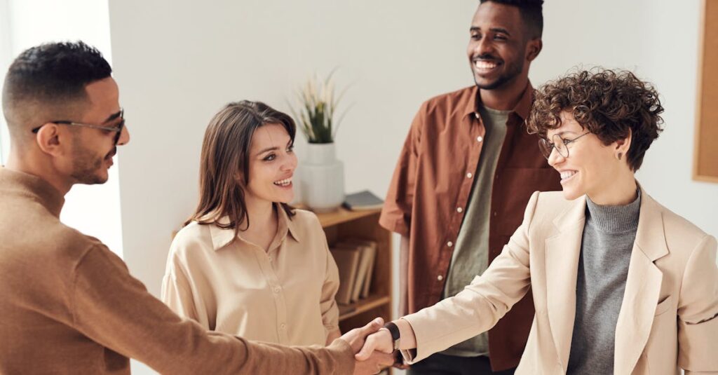 Four colleagues smiling and shaking hands in a bright office setting.